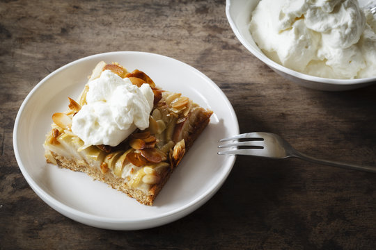 Piece of whole meal apple pie with sliced almonds and whipped cream