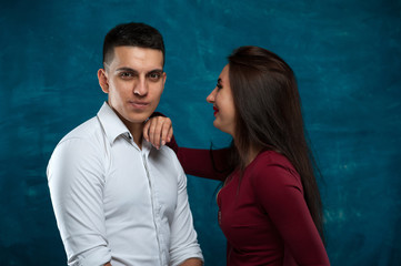 Young loving couple - man wearing white shirt and woman in deep red cloth posing on blue background