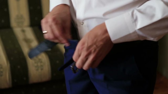 The stylish groom tucking his shirt into the trousers. Close-up view.