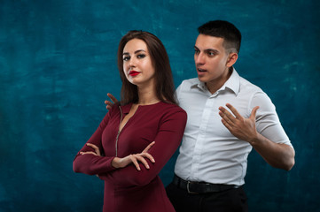 Happy young brunette woman looking at the camera and standing next to an angry man on blue background