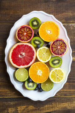 Plate of blueberries, kiwis and sliced citrus fruits on wood