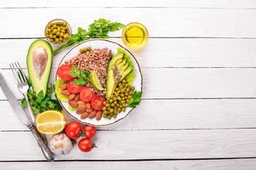Healthy food. Buckwheat, cherry tomatoes, avocados, almonds and green peas. On a wooden background. Top view. Free space for your text.