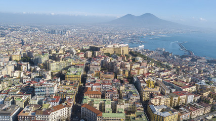 Fototapeta premium Aerial view of Naples from the Vomero district. You can see Castel Sant'elmo in the foreground while in the background the city's port, the Vesuvius and the Ovo castle. There are houses and buildings.