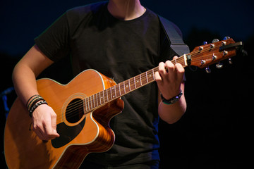 Macro shot of boy playing acoustic guitar on stage on evening. Band performing their songs. Music festivals in summer. Romantic acoustic melody.