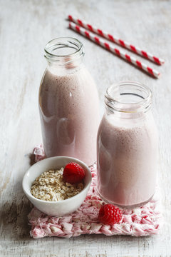 Glass bottles of raspberry milkshakes with oat flakes and basil