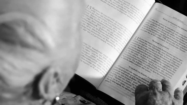 Elderly grandmother of eighty-three years is reading the Bible in the original in Greek in slow motion.