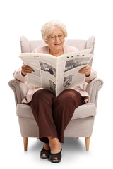 Elderly woman sitting in an armchair and reading a newspaper