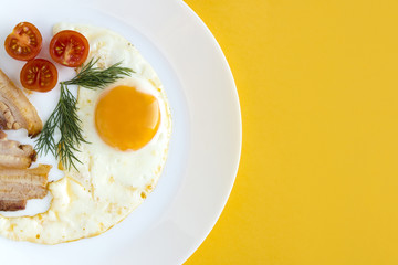 Fried eggs with tomatoes, bacon and dill. Delicious and healthy breakfast оn a white plate.