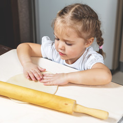 Little girl prepares the dough in the kitchen at home