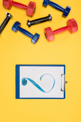 Sports dumbbells and clipboard isolated on yellow background