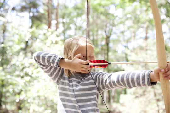 Girl shooting with bow and arrow in the forest