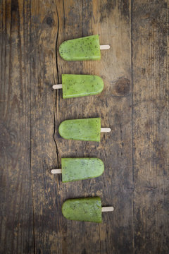Row of homemade kiwi ice lollies on dark wood