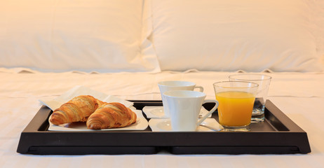 Breakfast in bed in a hotel room. Close up view of tray with croissant and juice. White background.