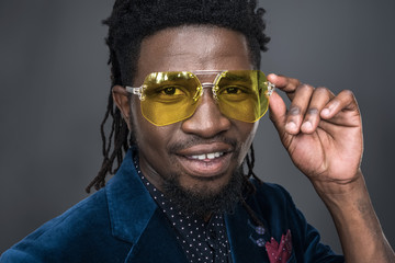 handsome african american man in yellow sunglasses looking at camera isolated on gray