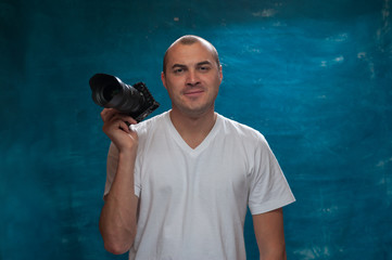 Portrait of smiling middle-aged man in white shirt with camera in his hands posing on blue background. Copyspace