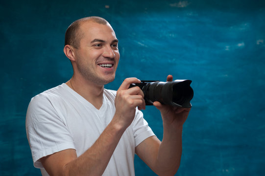 Portrait of smiling middle-aged man in white shirt with camera in his hands posing on blue background. Copyspace