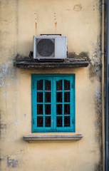 Fototapeta na wymiar Old green window with air compressor on yellow wall