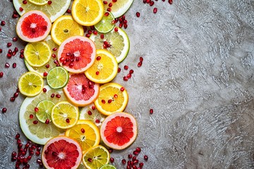 Sliced citrus fruits background (grapefruit, orange, lemon, lime) and pomegranate seeds on a rustic background, top view with copy space for your menu text.