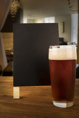Glass of beer and blackboard disposed on a bar of a restaurant.