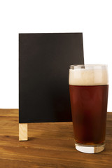 Glass of beer and blackboard disposed on wooden table, isolated on white background.