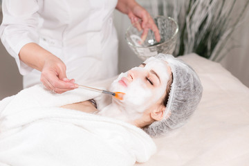 Obraz na płótnie Canvas Young pretty woman receiving treatments in beauty salons. Young beautiful dark-haired woman in the office beautician lying on the couch. Facial cleansing foam using.