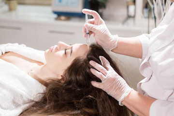 Handsome woman receives an injection in the head. The procedure makes doctor in white gloves. The concept of mesotherapy. Thrust to strengthen the hair and their growth