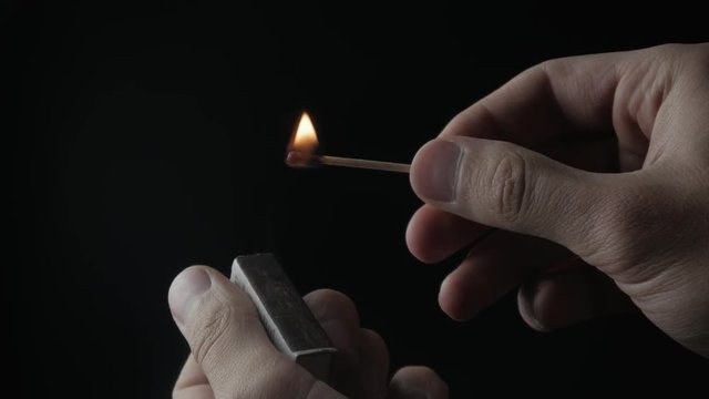 Striking wooden match and burning on black background.