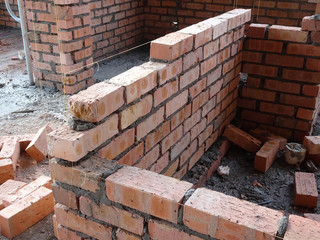 Construction workers laying clay bricks at the construction site to form a wall. The brick stick...