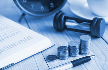 Blue theme color on stack of coin on the wood table with background clock and sandhour and book , finance concept.