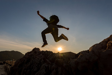 Silhouette of a jumper in the sea on a rocky seashore. Jumping on the beach at sunset with a warmth light