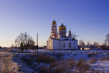 The Church of the Nativity in the Russian village of Lebyazhye on a winter evening and the dry grass on a snow-covered field.