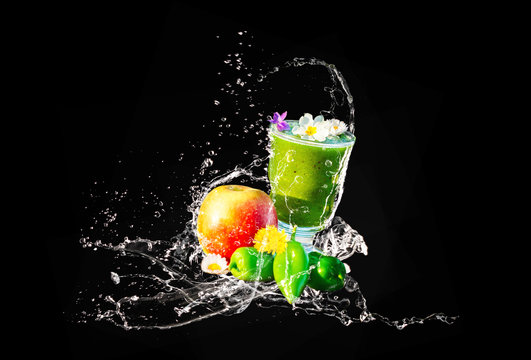 Gr&uuml;ner Smoothie mit essbaren Bl&uuml;ten und Fr&uuml;chten, Wasserspritzer, isoliert auf schwarz