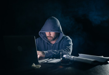 mysterious criminal man hacking laptop in the dark