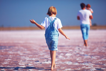 young boy in jeans romper walking through the pink salt lake, firth