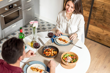 Happy young couple eating and drinking wine at home