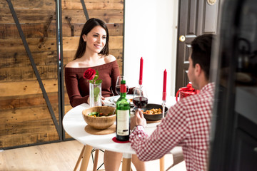Young happy couple celebrating Valentine's day with a dinner at home drinking wine, cheers.
