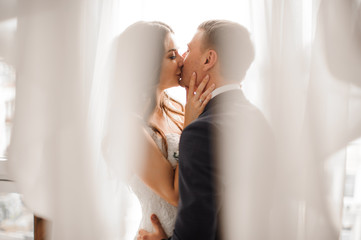 manly groom and beautiful bride kissing against white background