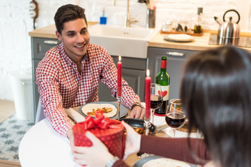 Young happy couple celebrating Valentine's day with a dinner at home drinking wine, cheers.