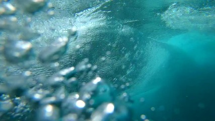 SLOW MOTION UNDERWATER: Crystal clear barrel wave breaking over camera in deep ocean. Camera descends from sunny beaches of Fuerteventura to deep crystal clear water below a large bubbling ocean wave. - Powered by Adobe