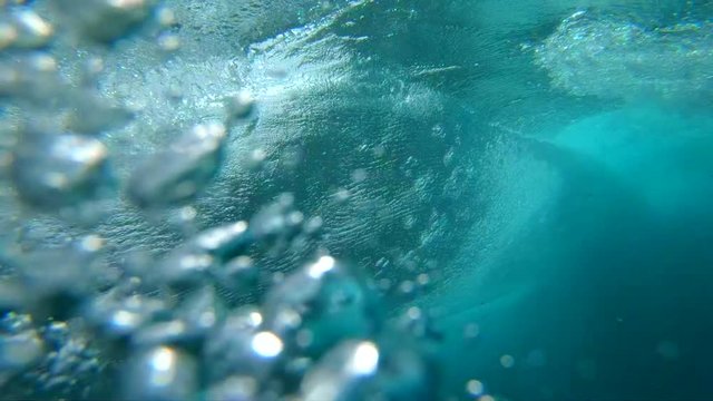 SLOW MOTION UNDERWATER: Crystal clear barrel wave breaking over camera in deep ocean. Camera descends from sunny beaches of Fuerteventura to deep crystal clear water below a large bubbling ocean wave.