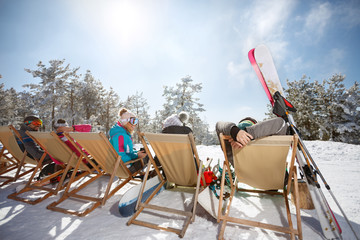 Friends on skiing sunbathing in sunbed on ski terrain, back view