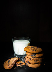 Stack of Chocolate chip cookies and glass of milk on dark wooden background. with copy space.
