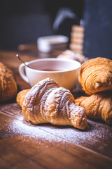Fresh croissants with sugar powder on a background of a cup with a spoon.