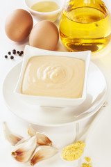 A bowl of homemade mayonnaise or aioli and its ingredients, oil, vinegar, eggs, black peppercorns, mustard and garlic.