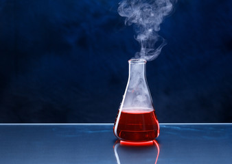 Erlenmeyer flask with red liquid on the tabel.  Experiment in the laboratory, smoke comes from...