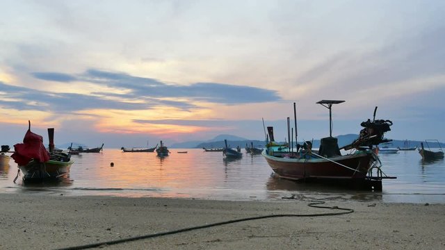 reflection of sunrise shining in Rawai sea fishing boats ready to fish. fishing boat parking near the beach waiting for high tide