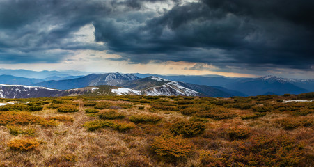 Panorama of idyllic landscape in the spring mountains at sunshine. View of the snow-covered mountain peaks in the distance.