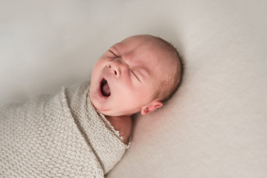 Newborn baby boy yawning while lying on the bed