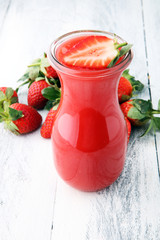 glass of strawberry smoothie and many fresh strawberries on a wooden background.
