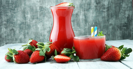 glass of strawberry smoothie and many fresh strawberries on a wooden background.